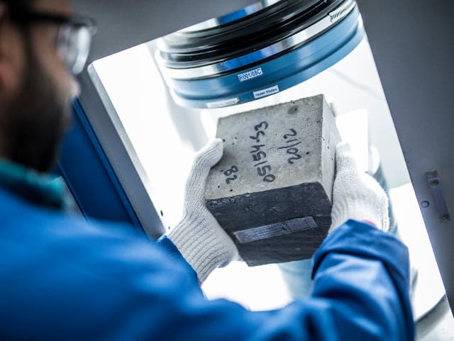 Construction site worker with hard hat and surveying equipment looking up at crane and preparing for building materials inspection