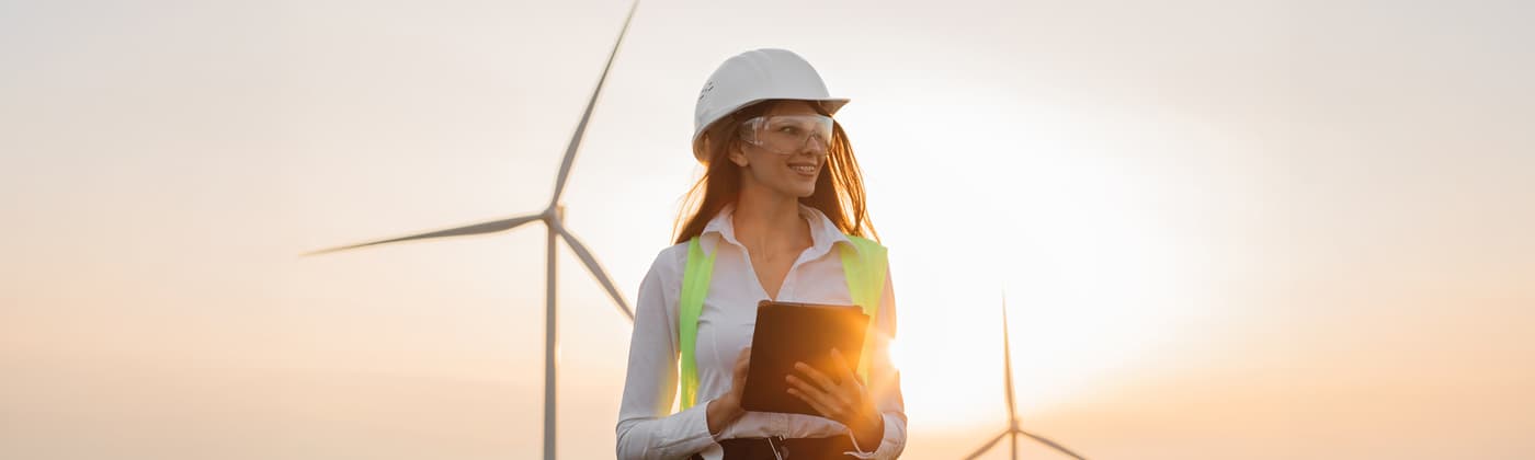 Environmental consultant in hard hat in field with wind turbines in background