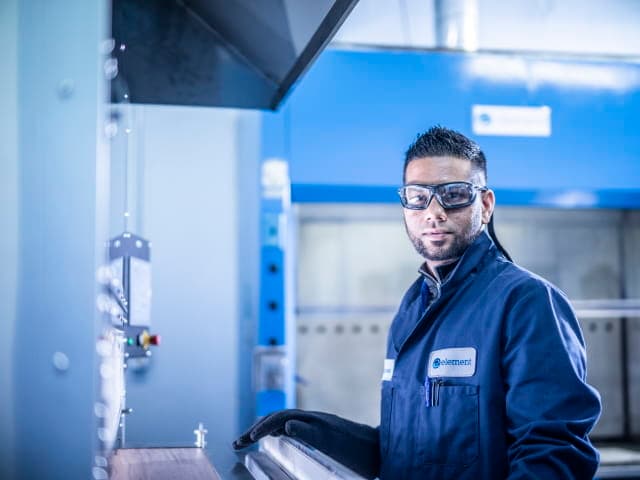 Element testing technician in blue lab coat standing in front of reaction to fire testing equipment